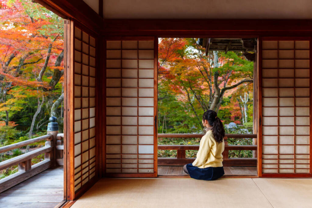 Young woman admiring autumn leaves from traditional Japanese terrace